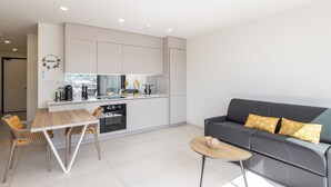 A modern kitchen with white cabinets, a dining table with chairs, a grey sofa with yellow pillows, and a small round table. - A105 - Breathtaking Apartment with Garden (Sint Maarten)