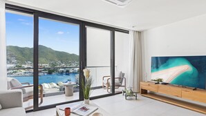 A modern living room with a large window, a flat-screen TV, and a view of a marina and mountains. - B246 - Breathtaking Lagoon View with Balcony (Sint Maarten)