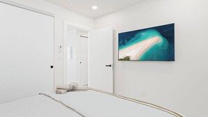 A modern bedroom with a bed, a painting of a beach, and a door leading to another room. - B246 - Breathtaking Lagoon View with Balcony (Sint Maarten)