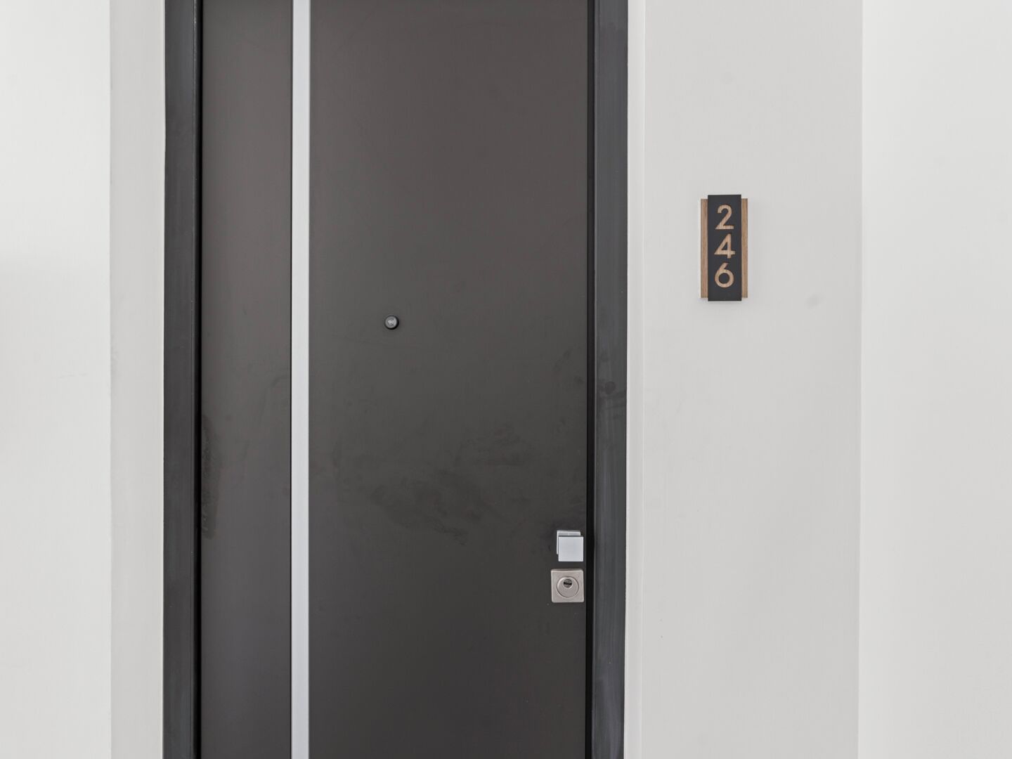 Une porte d’ascenseur de couleur sombre, dotée d’un petit interrupteur blanc et d’une plaque indiquant le numéro de la chambre : 246.