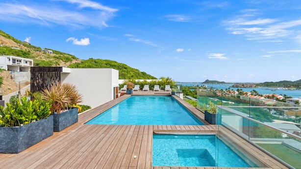 A rooftop infinity pool with wooden decking and lounge chairs, overlooking a coastal cityscape. - B246 - Breathtaking Lagoon View with Balcony (Sint Maarten)
