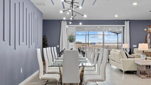 Un comedor moderno con una mesa de vidrio y sillas blancas, una lámpara de techo y vistas amplias por las ventanas.