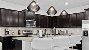 Una cocina moderna con armarios oscuros, una isla central con taburetes de bar, un refrigerador de acero inoxidable e iluminación colgante.