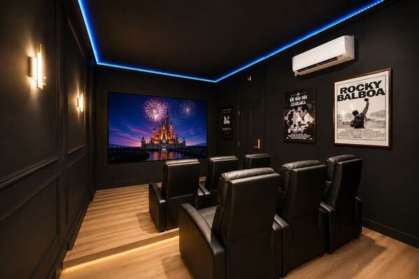 Una sala de cine con asientos de cuero negro, una pantalla grande mostrando un castillo y carteles en la pared.