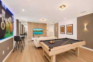 A modern living room with a pool table, a TV, a sofa, and a dining area. - Amazing Solara 7BR/ Pool /Spa /Free Waterpark (Kissimmee)