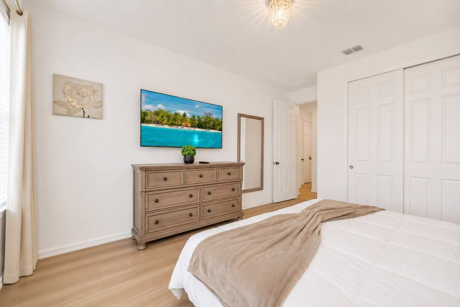 A bedroom with a bed, a dresser, a painting, and a door leading to another room.