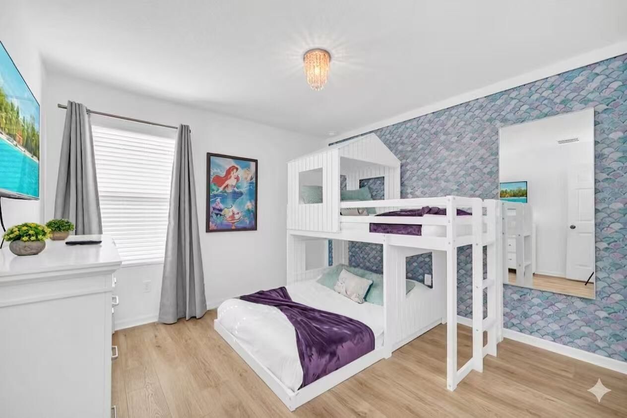 A bedroom with bunk beds, a desk, a chair, a TV, and a window with curtains.