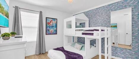 A bedroom with bunk beds, a desk, a chair, a TV, and a window with curtains.
