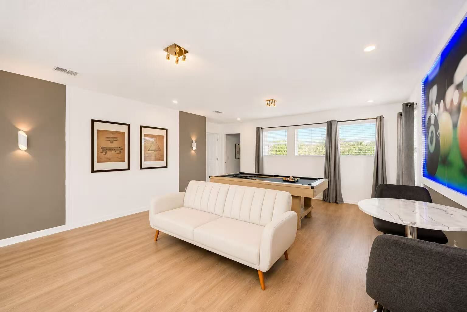A modern living room with a pool table, a sofa, and a dining area with a table and chairs.
