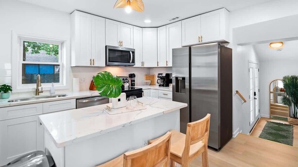 Una cocina moderna con armarios blancos, un refrigerador de acero inoxidable, un microondas y una isla grande con taburetes de bar.