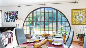 A dining area with a large arched window, a table set with breakfast, and a view of greenery outside.