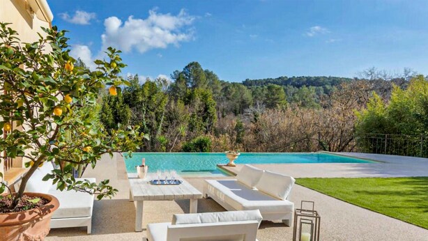 A poolside area with a white sofa set, a table, and a potted plant.