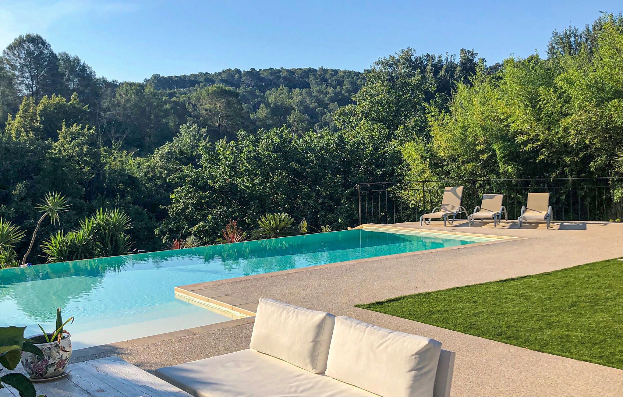 A swimming pool with lounge chairs and a grassy area, surrounded by trees and hills.