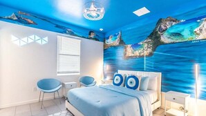 A bedroom with a bed, two chairs, a nightstand, and a wall mural of a coastal scene. - Brand New 15BR Mansion/Pool/Spa/Close to Disney (Kissimmee)
