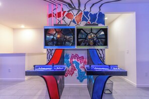 Quarto com duas estações de jogos, um mural na parede e uma televisão de tela plana.