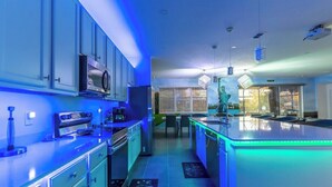 A modern kitchen with blue lighting, stainless steel appliances, and a central island. - Brand New 15BR Mansion/Pool/Spa/Close to Disney (Kissimmee)
