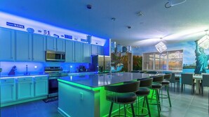 A modern kitchen with a central island, bar stools, and a mural of the Statue of Liberty. - Brand New 15BR Mansion/Pool/Spa/Close to Disney (Kissimmee)