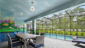 A covered patio with a dining table and chairs, a swimming pool, and a view of trees and grass. - Brand New Windsor Island 10BR Mansion/Pool/Spa (Davenport)