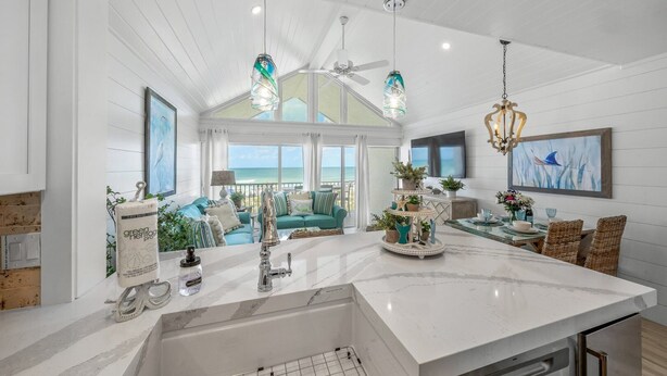 A spacious kitchen with a large island, a dining area with wicker chairs, and a view of the ocean through large windows.