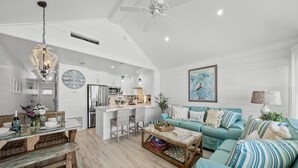 A spacious living room with a teal sofa, a wooden coffee table, and a dining area with a glass table and wicker chairs.