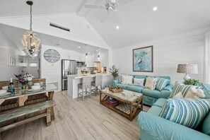 A spacious living room with a teal sofa, a wooden coffee table, and a dining area with a glass table and wicker chairs.
