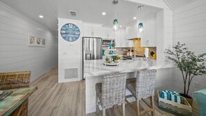 A modern kitchen with white cabinetry, a central island with bar stools, a clock, and a hanging light fixture.