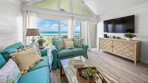 A spacious living room with a large TV, a wooden cabinet, and a view of the ocean.