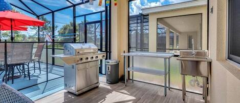 An outdoor patio with a grill, a sink, and a dining area with chairs and a table.