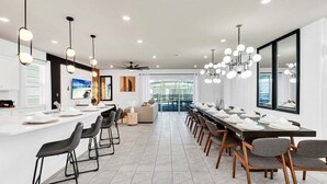 A modern dining area with a long table, multiple chairs, and pendant lighting. - Brand New Luxury 8BR Villa in Windsor Island (Davenport)
