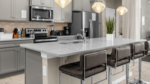 A modern kitchen with grey cabinets, stainless steel appliances, a central island with bar stools, and pendant lighting.