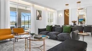 A modern living room with a sofa, armchairs, a coffee table, and a view of a lake. - Brand New Storey Lake 9BR Villa/Summer Kitchen (Kissimmee)
