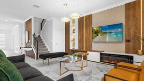 A modern living room with a fireplace, a staircase, and a large TV mounted on the wall. - Brand New Storey Lake 9BR Villa/Summer Kitchen (Kissimmee)