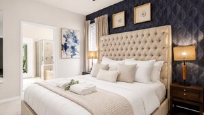 A bedroom with a tufted headboard, a large bed, a bedside table with a lamp, and a wall with framed artwork. - Amazing Windsor Island 7BR/Pool/Spa/closeTo Disney (Davenport)