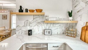 A modern kitchen with marble countertops, wooden shelves, and a built-in spice rack.