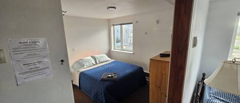 Een slaapkamer met een bed, een raam, een houten dressoir en een deur.