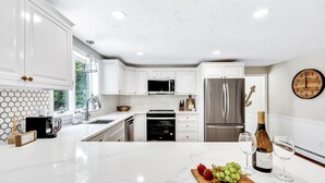 A modern kitchen with white cabinets, a marble countertop, and a clock on the wall. - Luxury retreat, in-ground huge pool, 10-person hot tub, outdoor shower, fire pit (Barnstable)