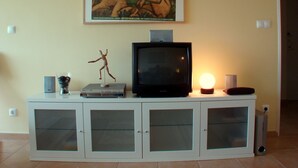 A living room with a television on a cabinet, a small statue, and a painting on the wall.
