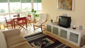 A living room with a sofa, a television, a painting, and a dining area with chairs and a table.