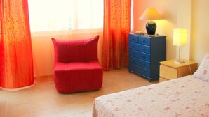 A bedroom with a bed, a dresser, a red chair, a lamp, and curtains.