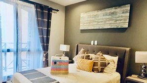 Ein Schlafzimmer mit einem großen Bett, einem Nachttisch, einer Lampe, einer dekorativen Tasche und Blick auf einen Balkon.