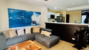 Ein Wohnzimmer mit einem grauen Ecksofa, einem Holztisch, einem Deckenventilator und einem großen abstrakten Gemälde.