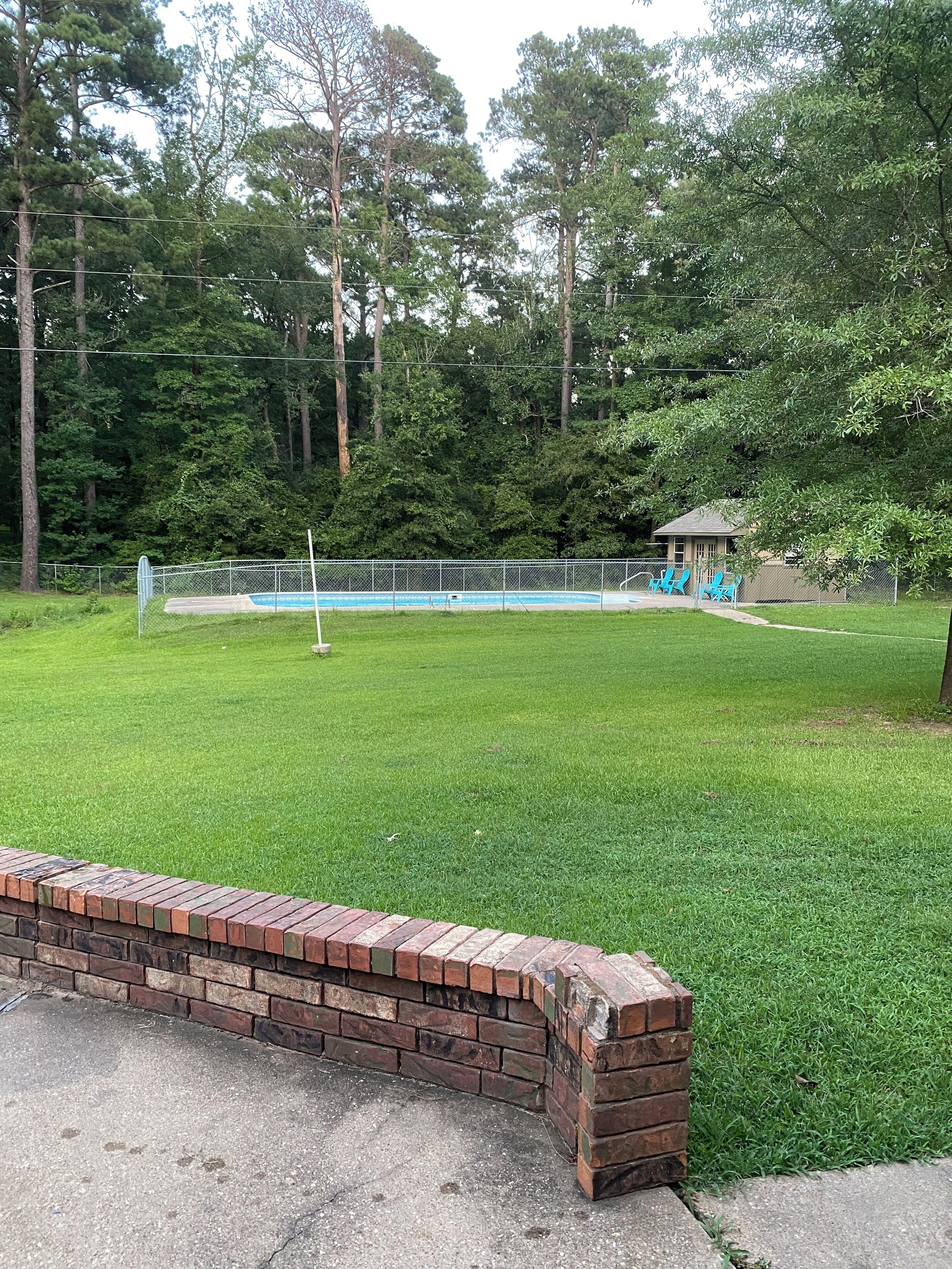 Une cour arrière clôturée avec une piscine, un mur en briques et un belvédère.