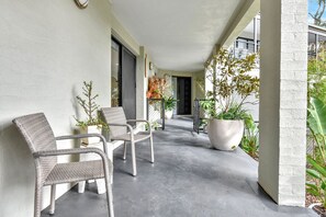 Ein überdachter Außenbereich mit zwei Korbstühlen, einem Blumentopf und einem Betonboden.