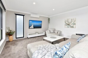 Een moderne woonkamer met een flatscreen televisie, een bank, een salontafel en een potplant.