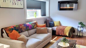 A living room with a sofa, a coffee table, a fireplace, and a window with blinds.