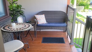 A covered porch with a wicker sofa, a round table, and a chair.