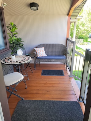 A covered porch with a wicker sofa, a round table, and a chair.
