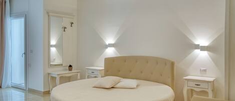 A modern bedroom with a round bed, two bedside tables, a mirror, and a ceiling light fixture.