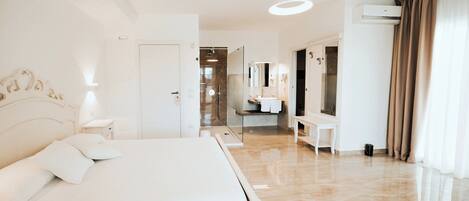 A hotel room with a large bed, a bedside table, a mirror, a bathroom with a sink and mirror, and a ceiling light.
