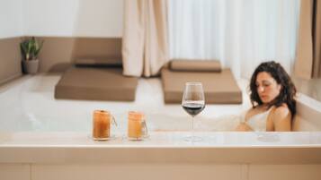 Uma banheira com velas, uma taça de vinho, uma planta e uma janela com cortinas.